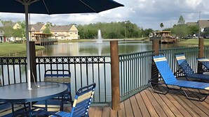 Une terrasse avec une table et des chaises, une fontaine, et une vue sur un lac et des bâtiments en arrière-plan.