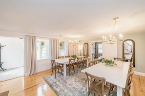 A dining area with a long table, multiple chairs, hanging plants, and a chandelier.