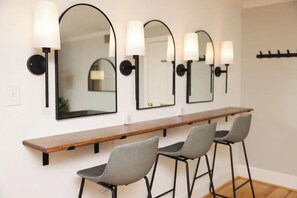 A modern bathroom with three mirrors, a wooden vanity, and two grey chairs.