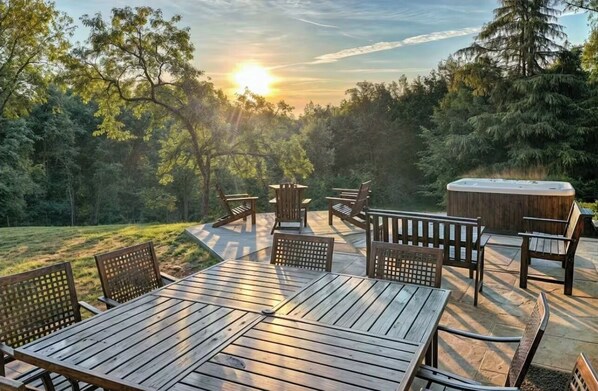 A deck with wooden furniture and a hot tub, surrounded by trees and a sunset view. - Spacious w/ 4 Suites, Hot Tub, Perfect for groups! (Altavista)
