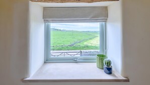 Una finestra amb vista a un camp verd i una paret de pedra.