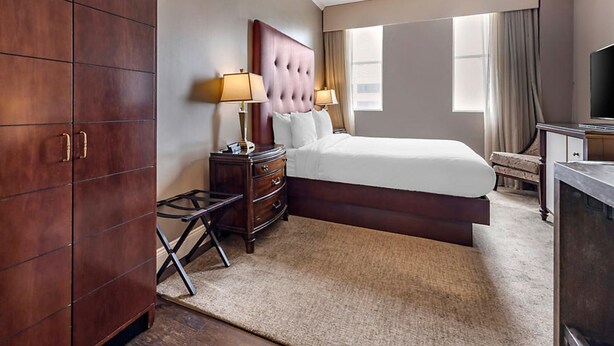 Una habitación de hotel con una cama grande, dos mesitas de noche con lámparas, un armario y un televisor.