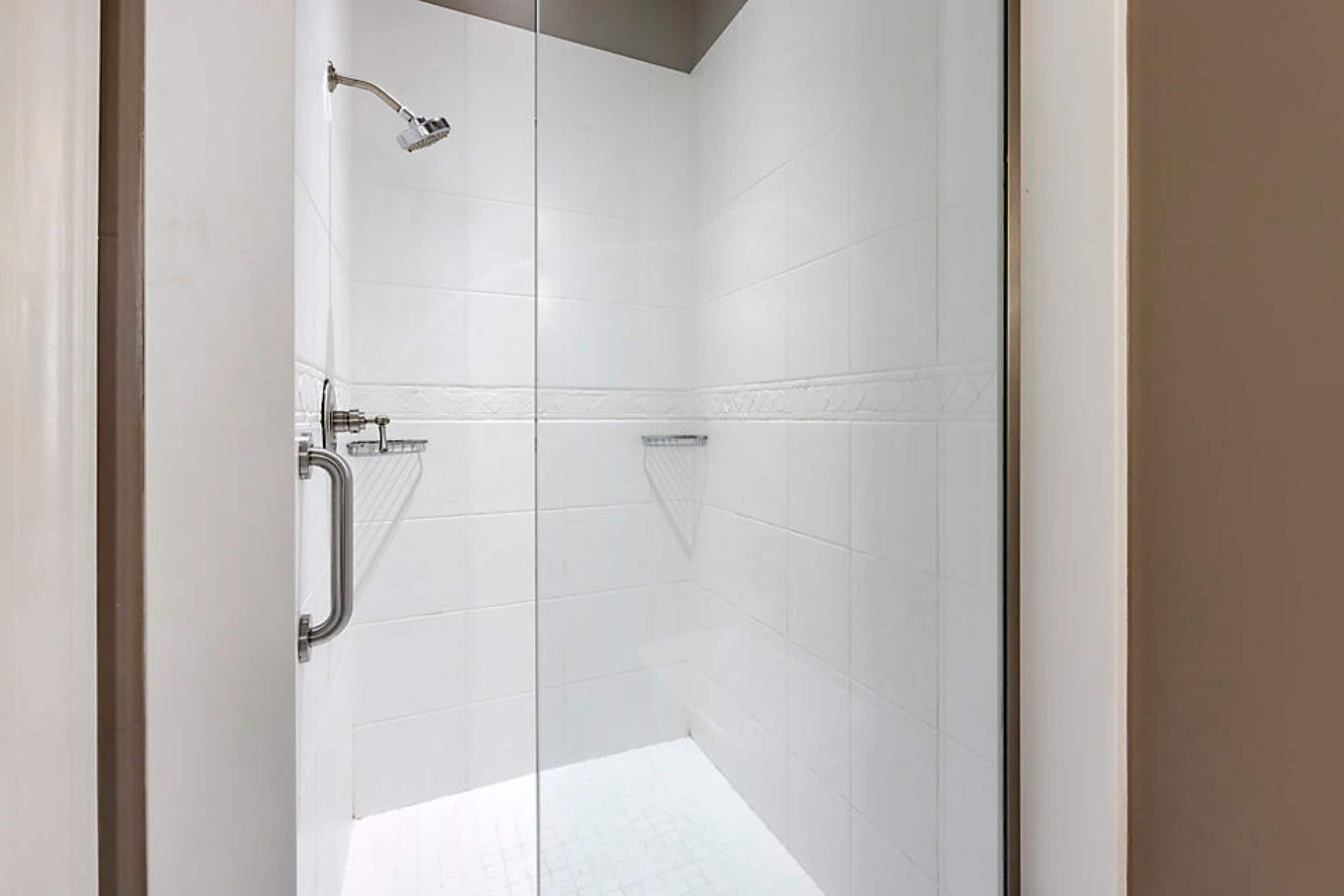 A modern bathroom with white tiles, a glass shower enclosure, and a handrail.