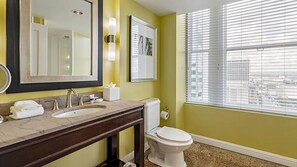 A bathroom with a large mirror, two sinks, a toilet, and a window with blinds.