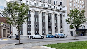 Un edificio de arquitectura clásica, aceras y vehículos estacionados.