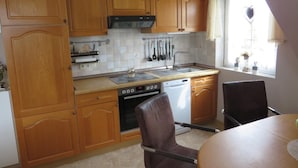 Une cuisine dotée de meubles en bois, d’une cuisinière, d’un lave-vaisselle et d’un coin repas avec une table et des chaises.