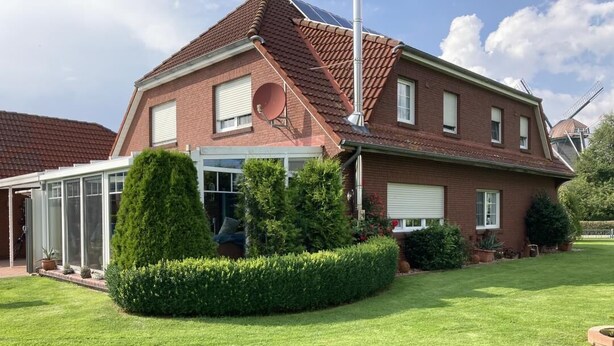 Une maison à deux étages, construite en briques, dotée d’une antenne parabolique, d’une véranda et d’une pelouse bien entretenue.