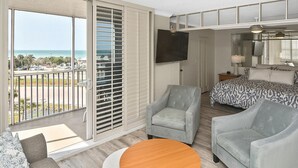 Ein Zimmer mit Balkon, einem Bett, einem Fernseher und einer Sitzecke mit Tisch.