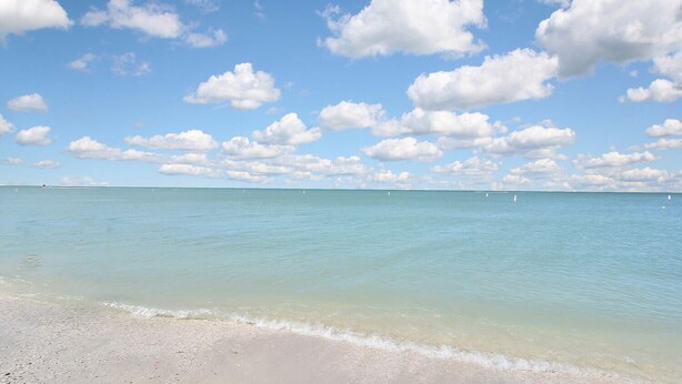 Ein Strand mit klarem türkisfarbenem Wasser und einem Sandstrand unter blauem Himmel mit vereinzelten Wolken.