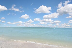 Ein Strand mit klarem türkisfarbenem Wasser und einem Sandstrand unter blauem Himmel mit vereinzelten Wolken.