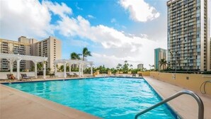 A swimming pool with lounge chairs and a pergola, surrounded by high-rise buildings. - New Listing Ocean View Studio (Honolulu)