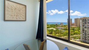 A room with a large window offering a view of a cityscape and a beach. - New Listing Ocean View Studio (Honolulu)