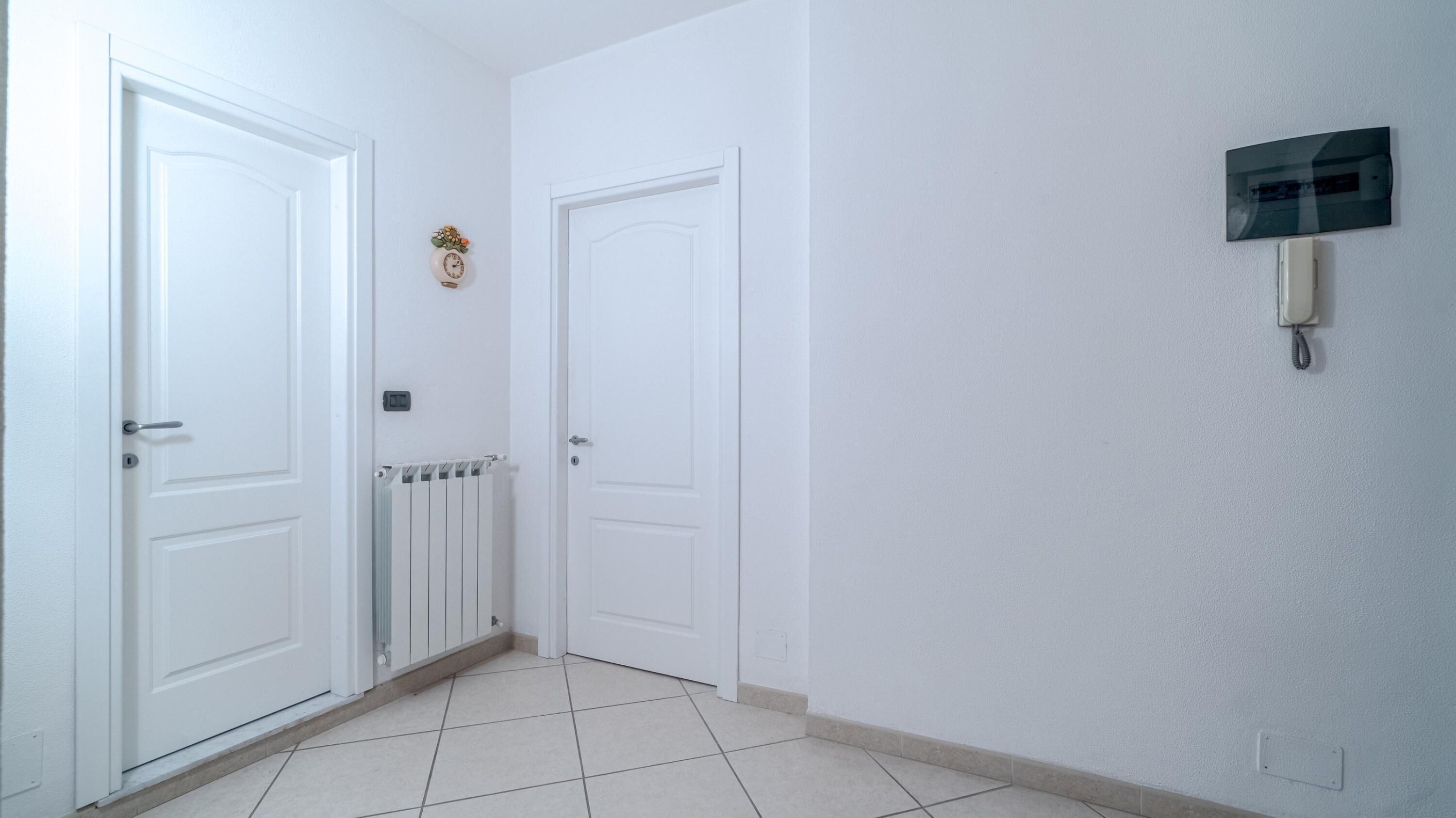 A hallway with white doors, a radiator, and a wall-mounted intercom.