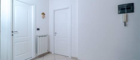 A hallway with white doors, a radiator, and a wall-mounted intercom.