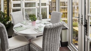 A conservatory with a round table, wicker chairs, and a potted plant. - 2 bedroom accommodation in East Woodburn (East Woodburn)