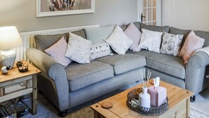A living room with a grey sofa, multiple cushions, a wooden coffee table, a lamp, and a framed artwork on the wall. - 2 bedroom accommodation in East Woodburn (East Woodburn)