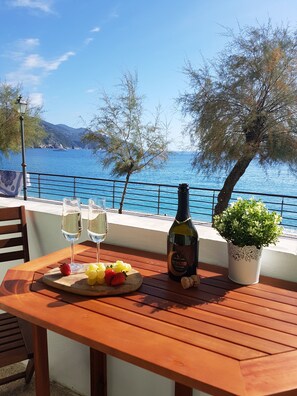 A wooden table with two glasses of white wine, a bottle of rosé, and a fruit platter with grapes and strawberries. - Mori's Beautiful Sea front Apartment - With A/C (Monterosso al Mare)
