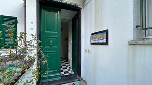 Una puerta verde con un pequeño porche, acceso con baldosas y un letrero en la pared.