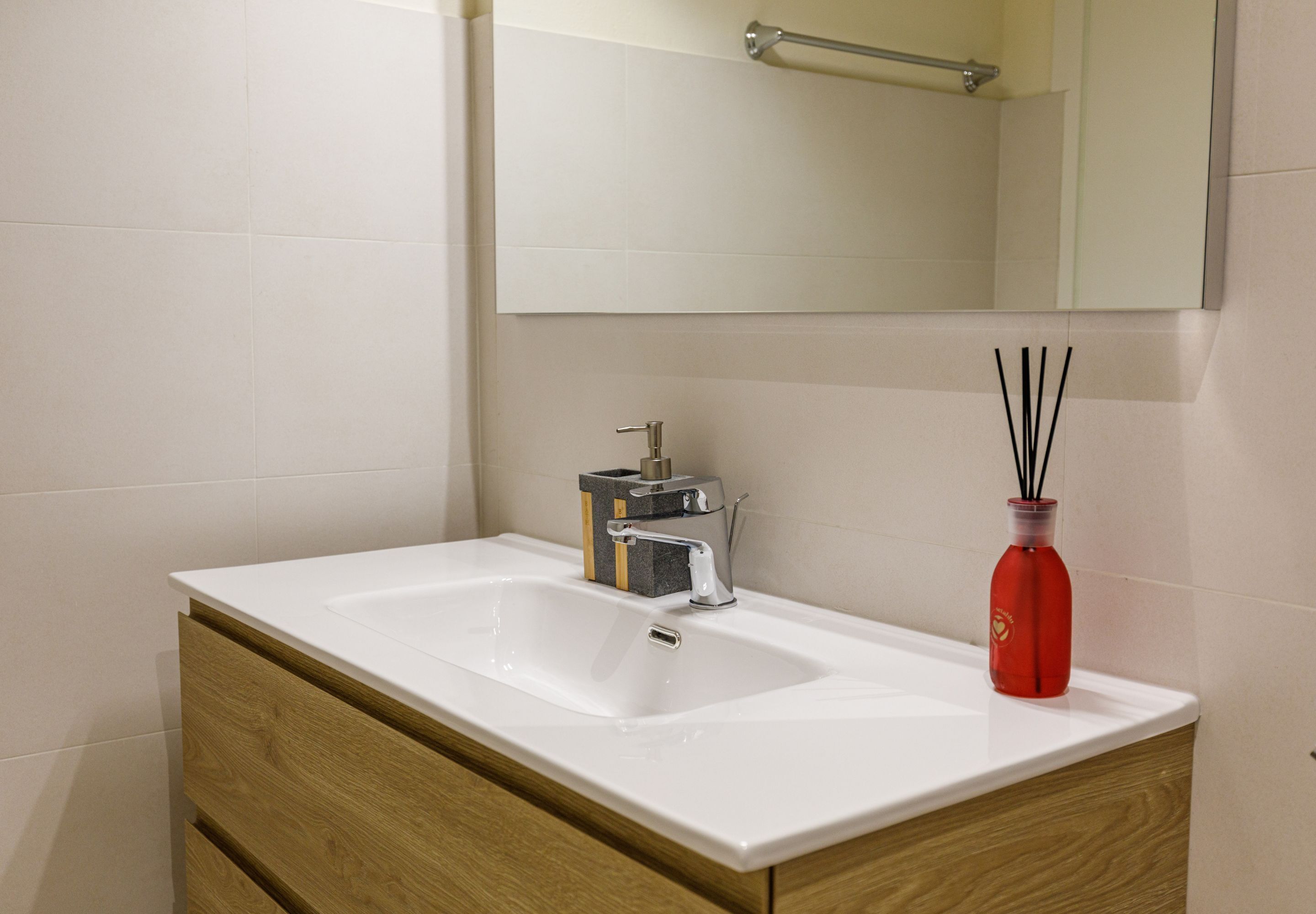 A bathroom with a white sink, wooden cabinet, and a mirror above the sink.