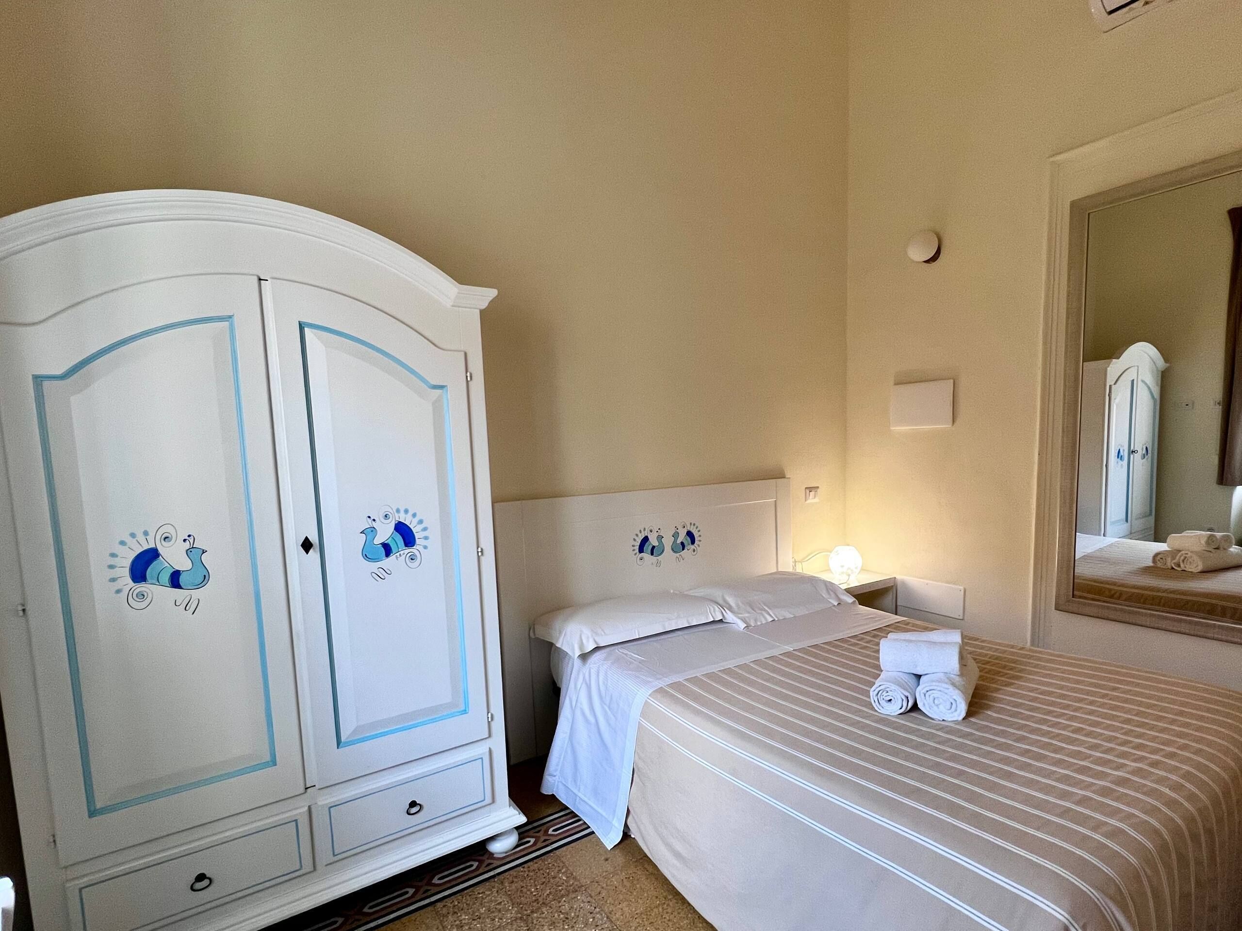 Una habitación de hotel con una cama, un armario, una mesita de noche con una lámpara y un espejo en la pared.
