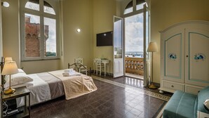 A hotel room with a bed, a desk, a chair, a wardrobe, and a balcony with a view of a building. - Onlyrooms IV - Sea View & Free Parking (Cagliari)