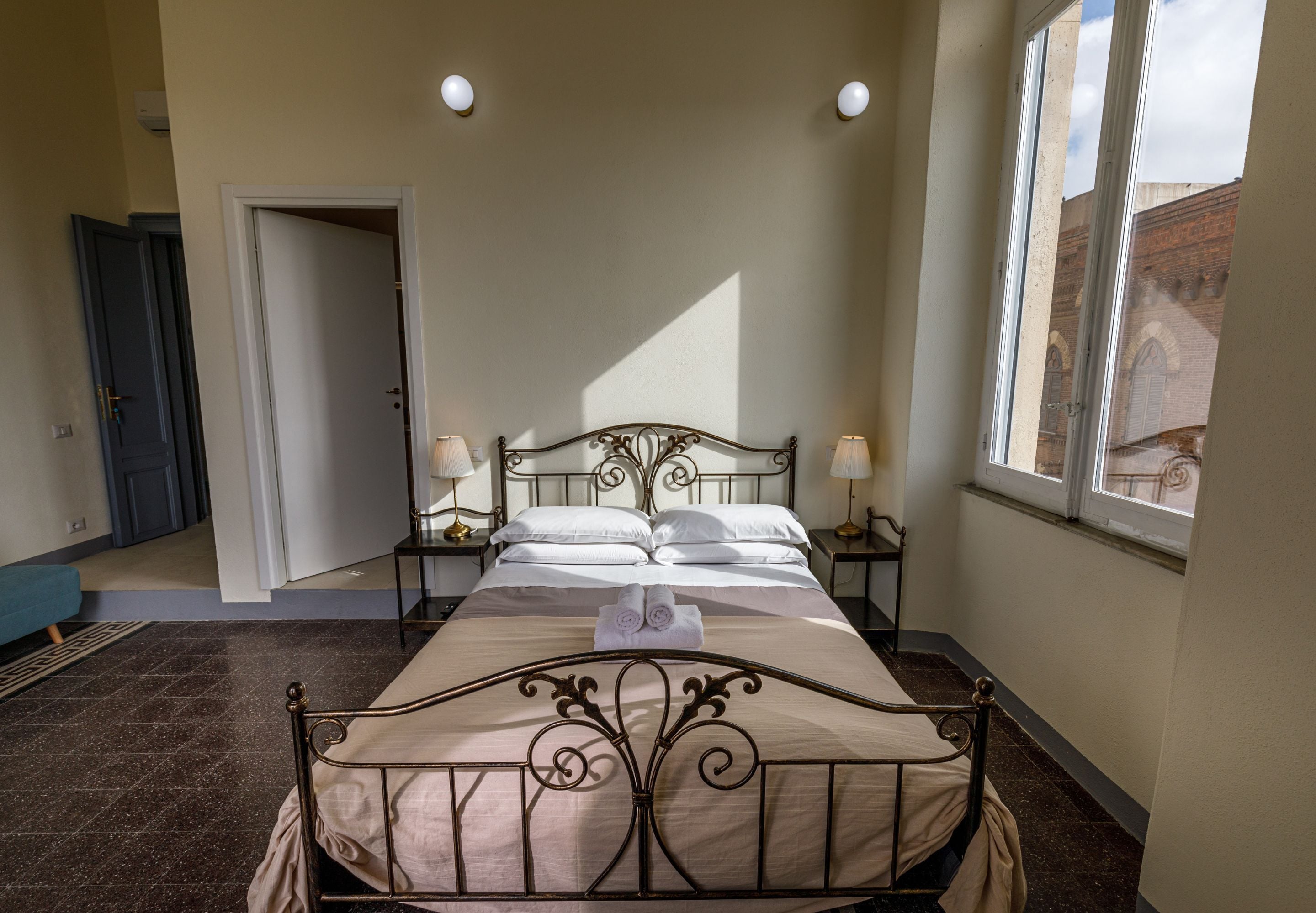 Quarto bem arrumado com uma cama grande, luminárias de cabeceira e vista para um edifício pela janela.