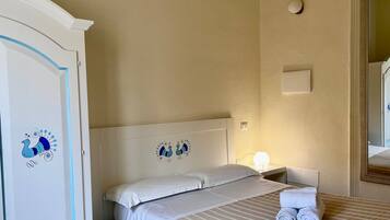 A hotel room with a bed, pillows, a nightstand, a lamp, and a wardrobe.
