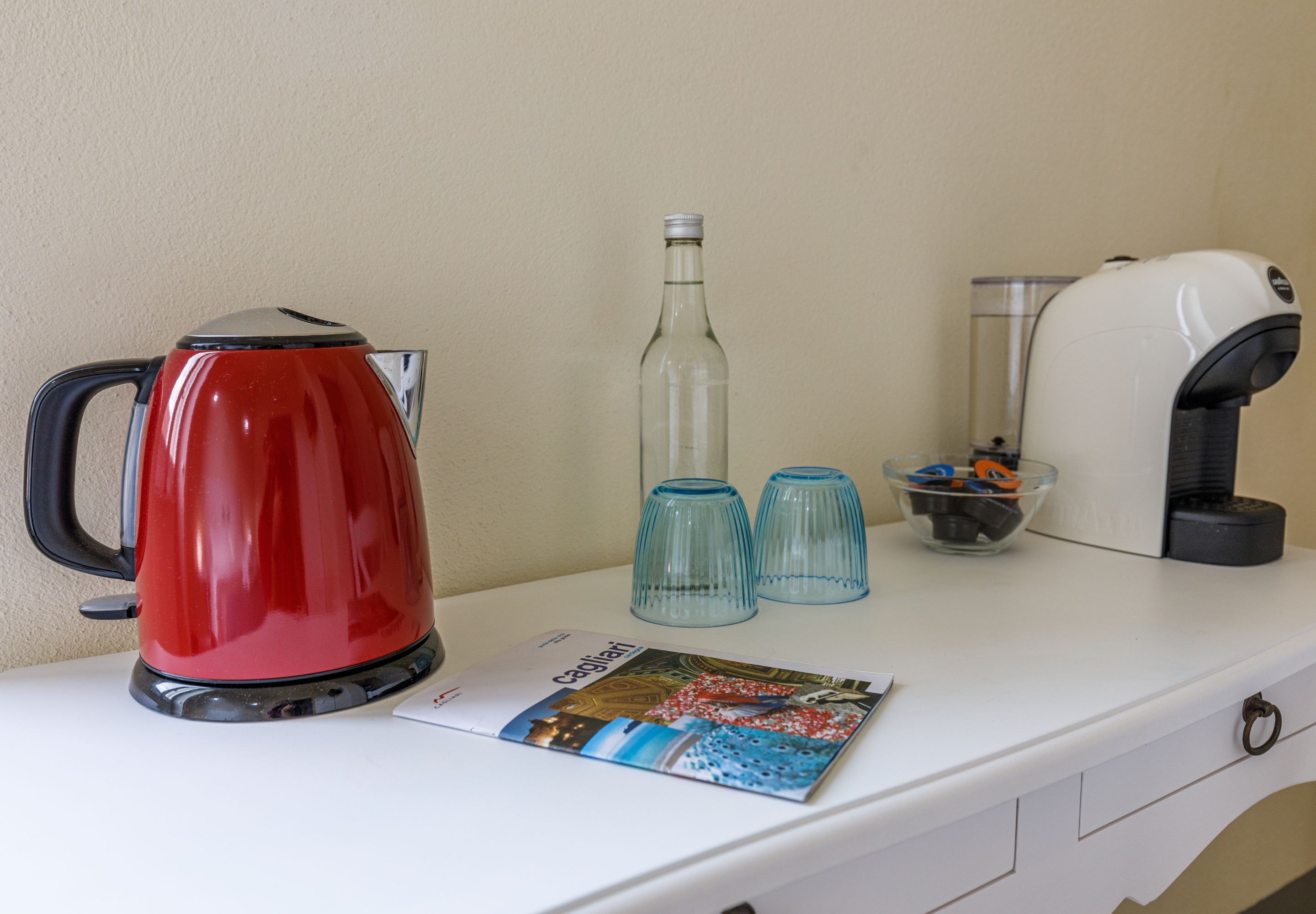 Un plan de travail de cuisine avec une bouilloire rouge, deux verres bleus, une bouteille et une machine à café.