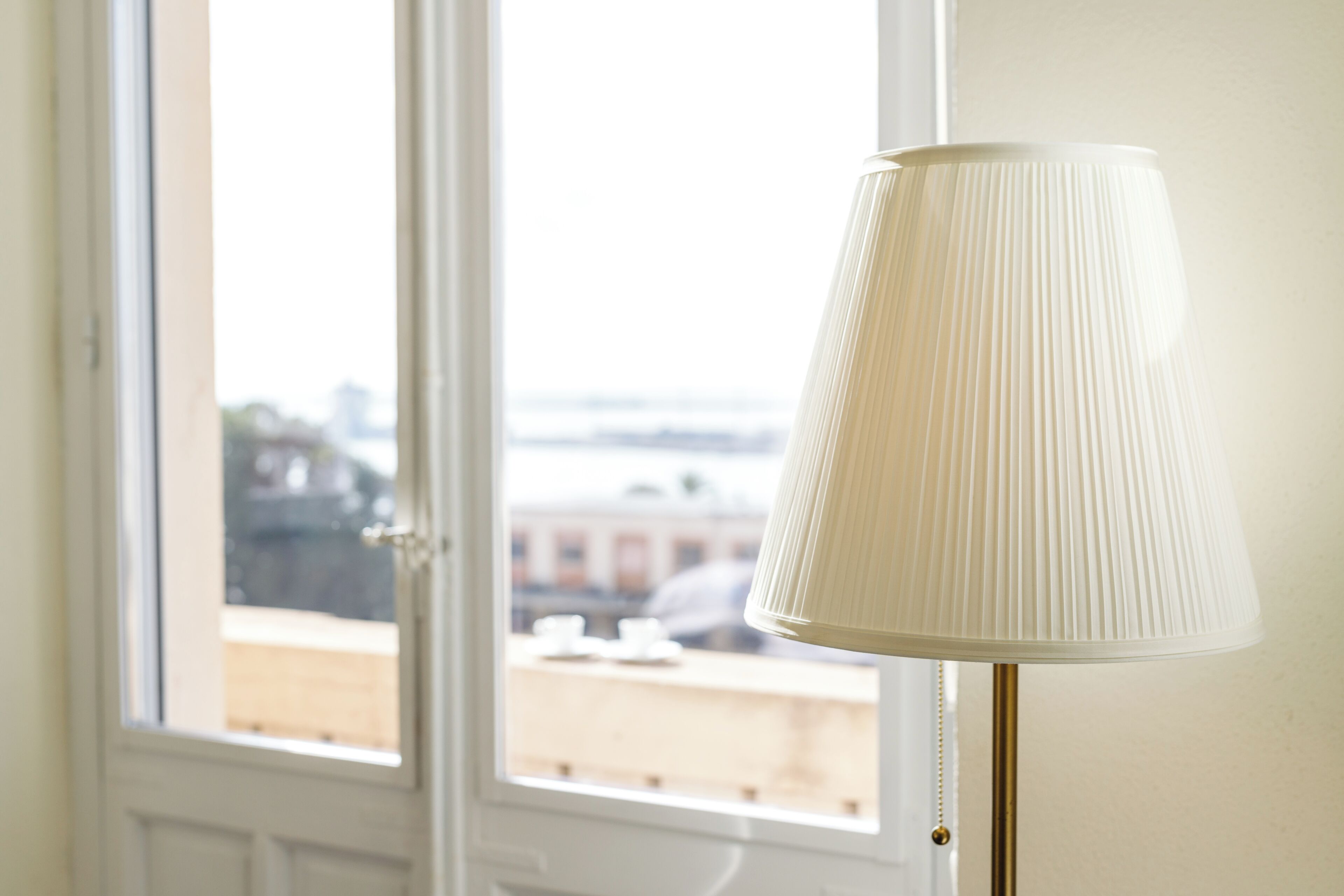 A room with a window, a white lamp, and a view of buildings outside.