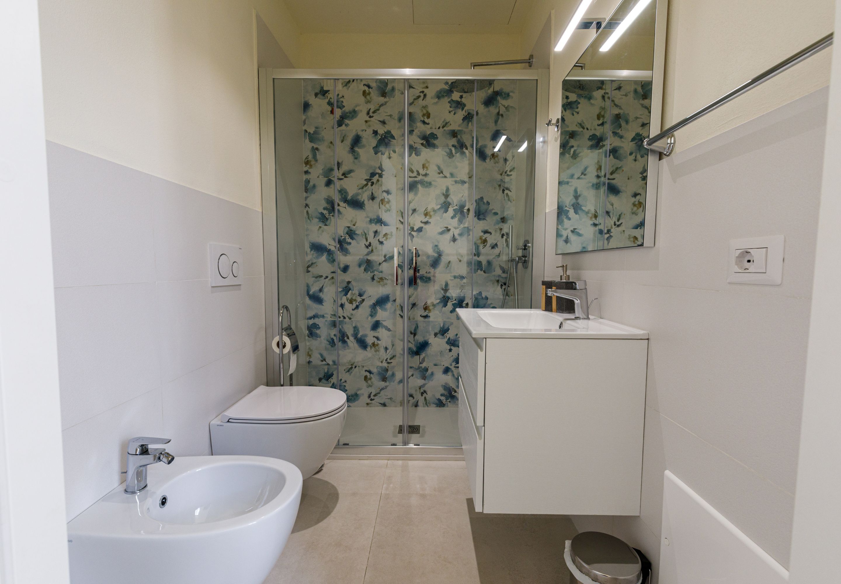 A bathroom with a bidet, toilet, and a glass-enclosed shower area.