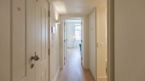 A narrow hallway with white doors on both sides, leading to a room with a window and a blue chair.