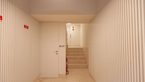 A narrow hallway with a door on the left and a staircase leading to an elevator on the right.