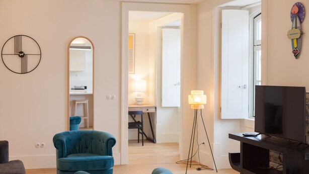 A living room with a TV, two blue armchairs, a lamp, and a mirror.