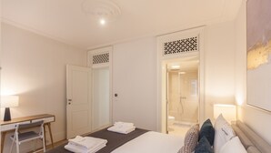 A hotel room with a bed, a desk, and a shower area.
