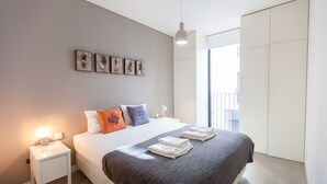 Um quarto moderno com uma cama bem arrumada, uma mesa de cabeceira com abajur e uma obra de arte na parede.
