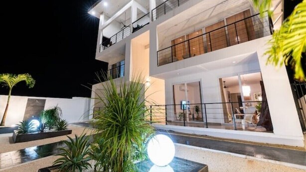 Un moderno edificio a più piani con balconi, ampie finestre e uno spazio esterno luminoso con piante e un elemento d'acqua.