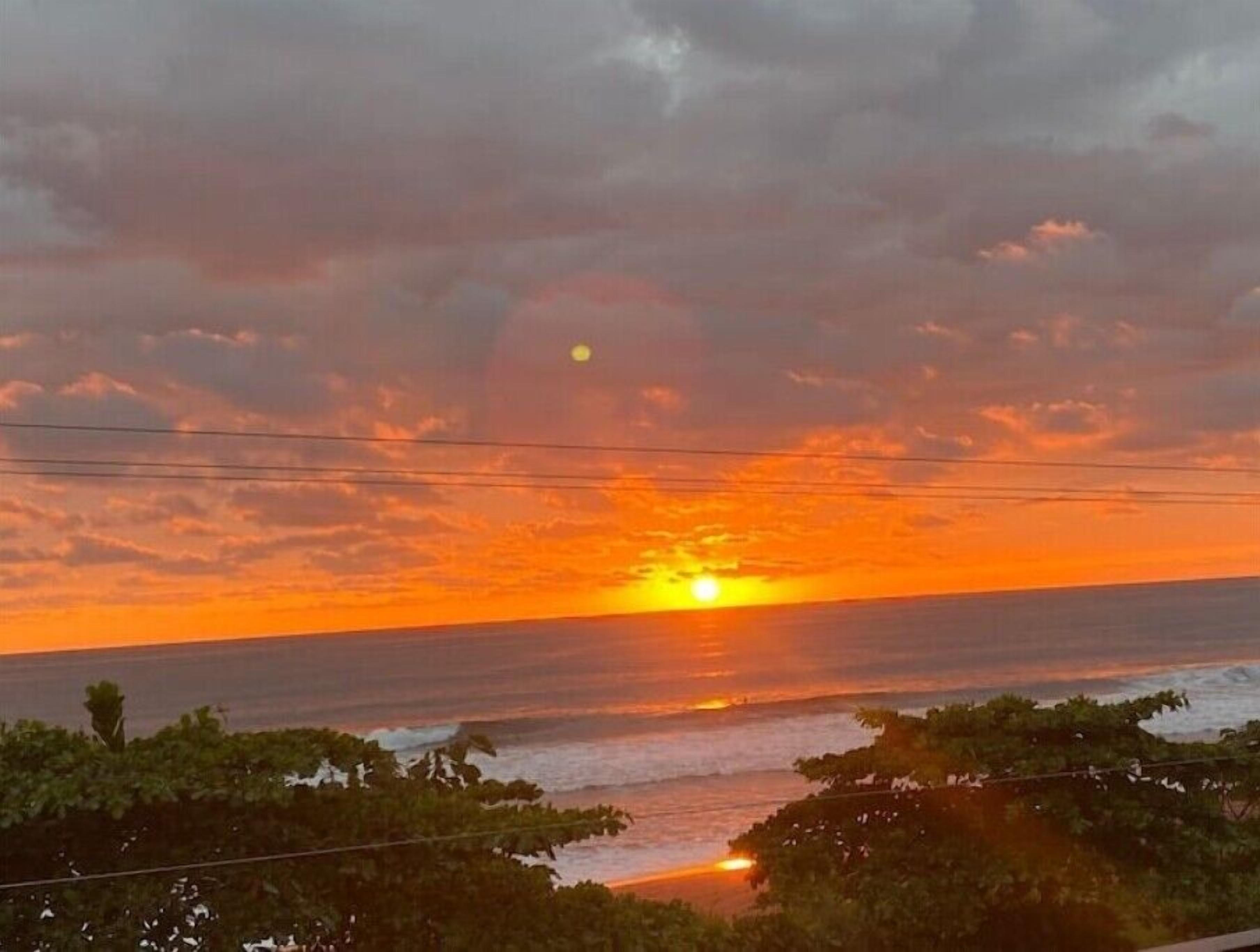 Un coucher de soleil sur l’océan, avec un ciel dégagé et quelques nuages.
