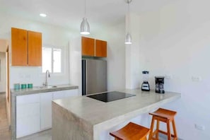 Une cuisine moderne avec des meubles blancs, un réfrigérateur en acier inoxydable, une plaque de cuisson à induction noire et des tabourets en bois.