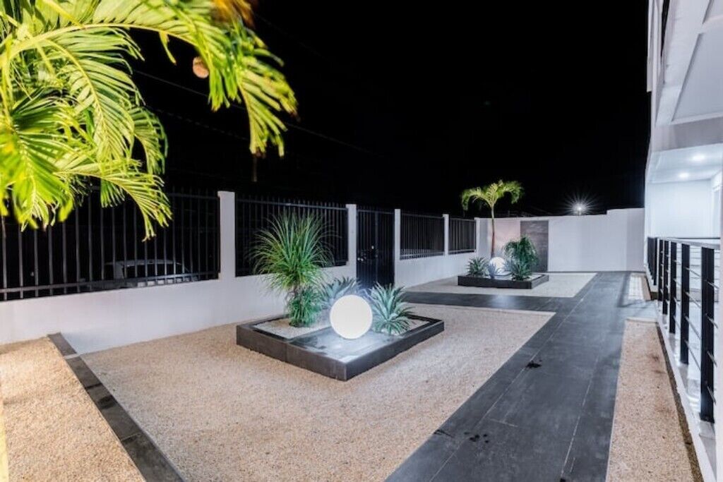 Eine Dachterrasse im minimalistischen Stil mit einer zentralen Leuchte, Topfpflanzen und einem Metallgeländer.