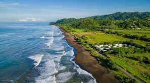 Paesaggio costiero con spiaggia, vegetazione e alcuni edifici sparsi.