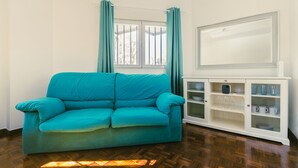 A teal sofa in a room with a wooden floor, a white cabinet with glass doors, and a large mirror on the wall. - Madrid Rio Perfect location for exploring Madrid! Modern 1-bed flat sleeps 2. (Madrid)