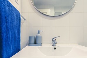 Ein Badezimmer mit einem weißen Waschbecken, einem runden Spiegel und einem blauen Handtuch.