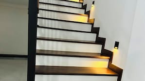 Eine Treppe mit Holzbodenstufen und schwarzen Geländern, beleuchtet durch an Wänden befestigte Lampen.