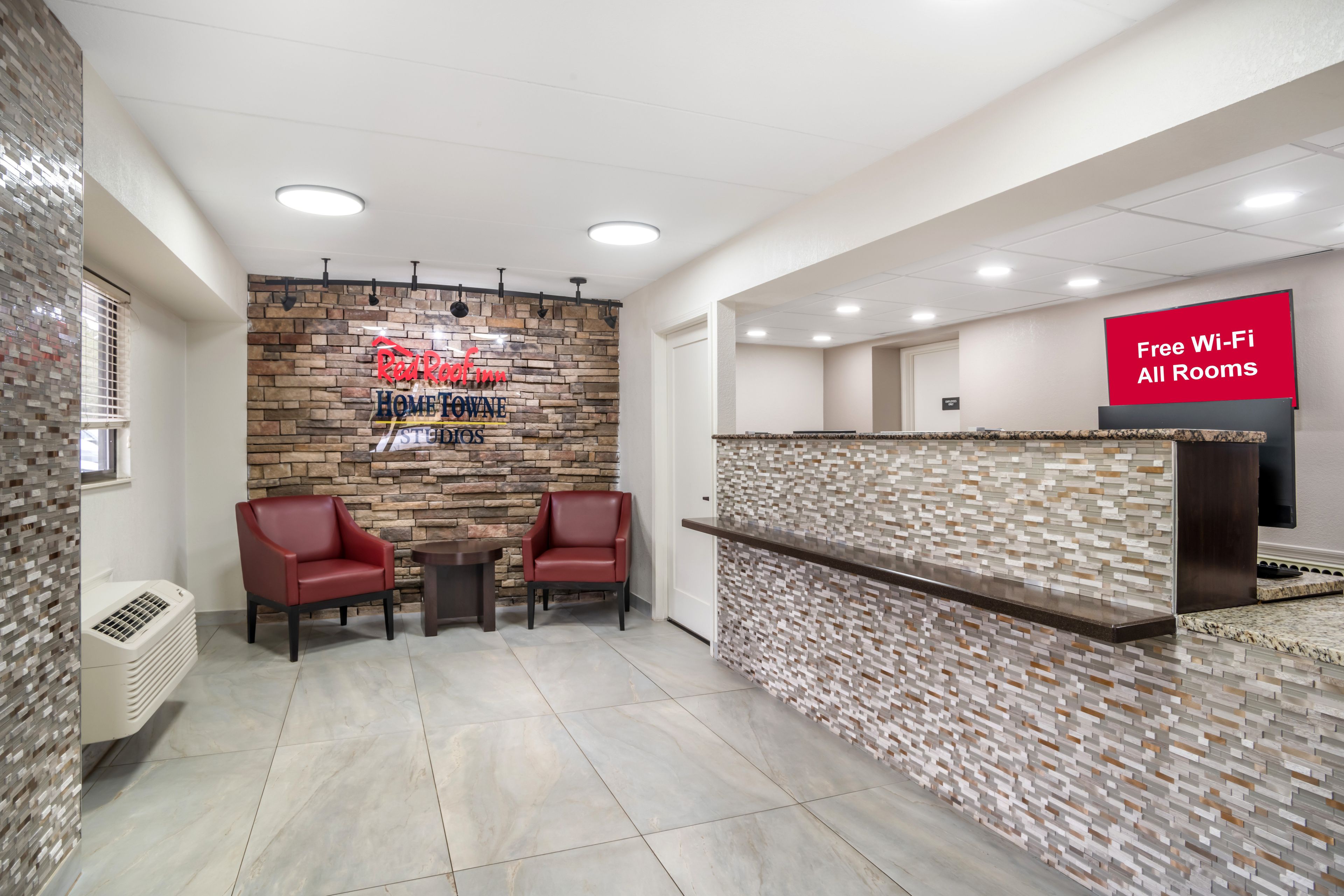 A hotel reception area with a stone wall, two red chairs, a small table, and a sign offering free Wi-Fi.