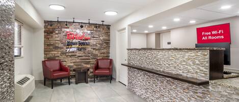A hotel reception area with a stone wall, two red chairs, a small table, and a sign offering free Wi-Fi.