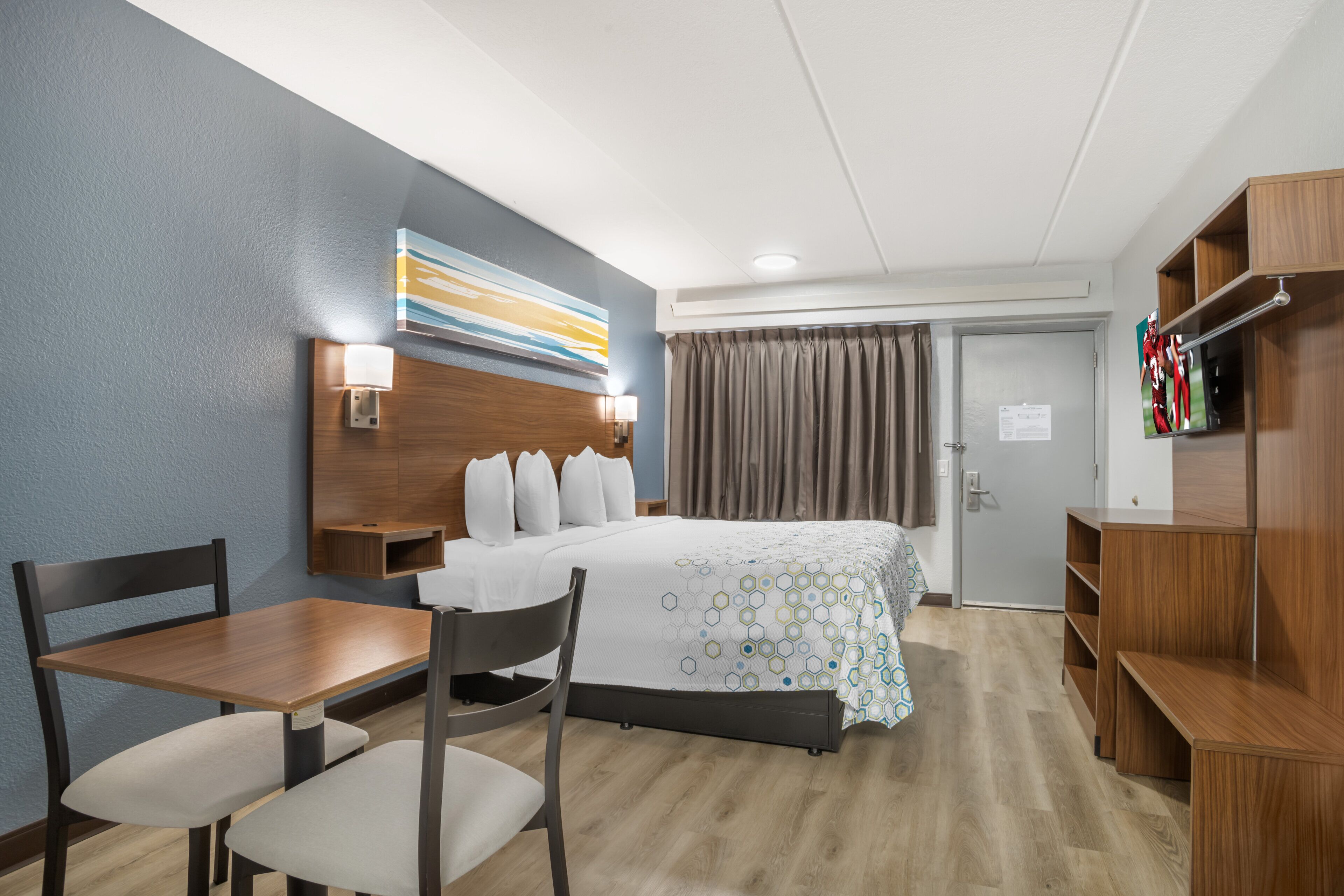 Une chambre d’hôtel comprenant un lit, un bureau, deux chaises, une télévision et une armoire.