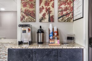 Een kitchenette met een koffieapparaat, een heetwaterdispenser en een bekerhouder.