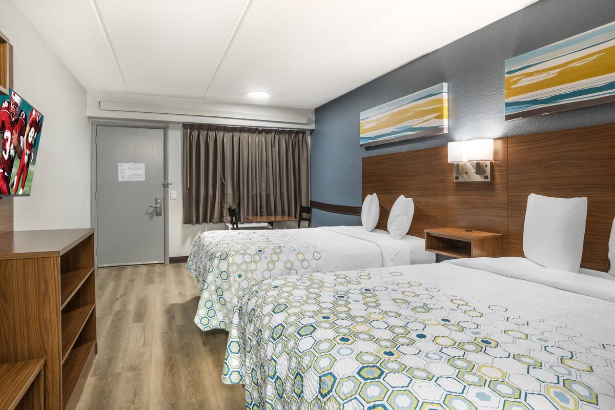 Une chambre d’hôtel avec deux lits, un bureau en bois, une télévision et une salle de bain avec un rideau de douche.