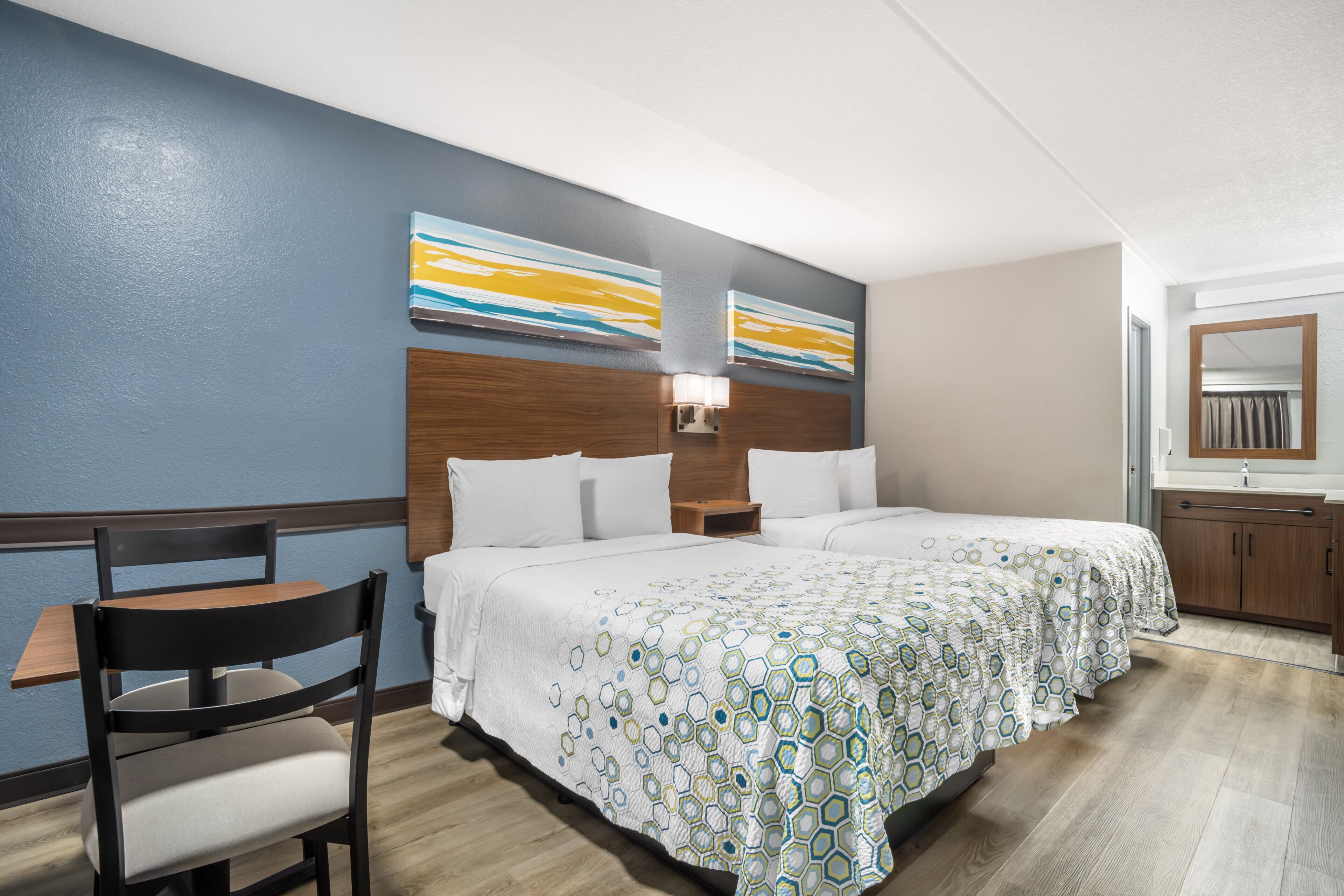Habitación de hotel con dos camas, un escritorio, una silla y obras de arte en las paredes.