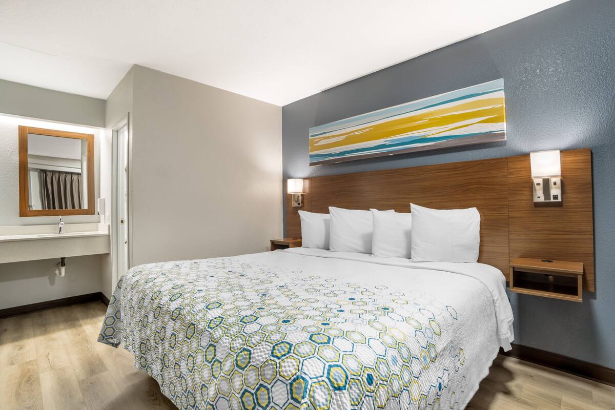 Une chambre d’hôtel avec un grand lit, une tête de lit en bois, un téléviseur fixé au mur et une table de chevet.